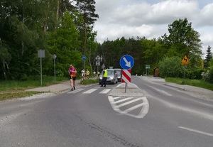 Trasa biegu. Policjant zatrzymuje ruch samochodów, by zawodnicy mogli bezpiecznie przebiec.