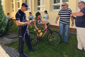policjant wypełnia dokumentacje, a obok niego stoi dziewczynka z rowerem