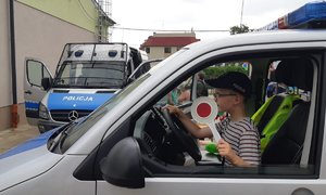 Dziecko siedzi za kierownicą radiowozu trzymając w ręku policyjny tzw. &quot;lizak&quot;.