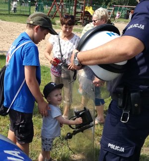 Policjant prezentuje dzieciom tarczę policyjną oraz hełm.