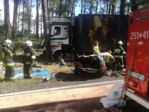 strażacy stoją przy uszkodzonym pojeździe ciężarowym