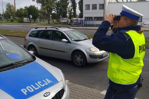 policjant obserwuje przez lornetkę kierowców, którzy korzystają z telefonu komórkowego podczas jazdy