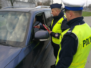 Policjanci wręczają ulotki kierowcy auta.