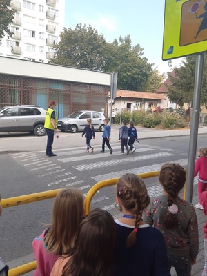 dzieci przechodzą przez przejście dla pieszych, a policjanta wstrzymuje ruch na ulicy
