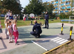 Policjanci prowadzą zajęcia z przedszkolakami na terenie zielonym. Wykorzystują do tego miasteczko ruchu drogowego.