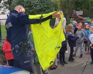 Policjant prezentuje dzieciom kamizelkę odblaskową.