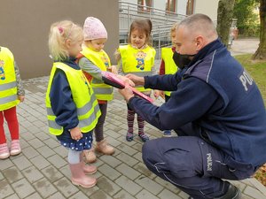 policjant kucając wręcza dzieciom opaski odblaskowe