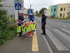 Policjant instruuje dzieci stojące przy przejściu dla pieszych.