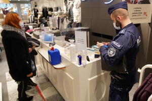 policjant i dwie pracownice sanpeidu kontrolują jeden z sklepów w galerii handlowej. Policjant sprawdza dane