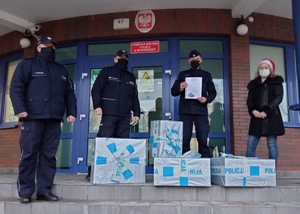 Policjanci stoją na schodach Komendy Miejskiej Policji w Bydgoszczy. Przed nimi leżą paczki z darami dla dzieci ze szpitala.