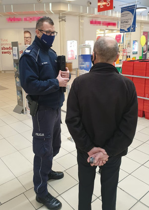 Policjant rozmawia z seniorem na terenie placówki handlowej.