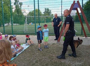 Policjanci z psem służbowym prowadzą prelekcję dla dzieci.