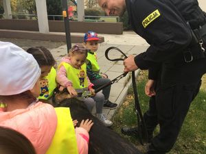 Dzieci pod okiem policjanta bawią się z psem policyjnym.