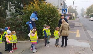 Dzieci wraz z policjantem i Polfinkiem idą w stronę przejścia dla pieszych.