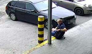 Mężczyzna siedzący obok zaparkowanego samochodu rozgląda się.